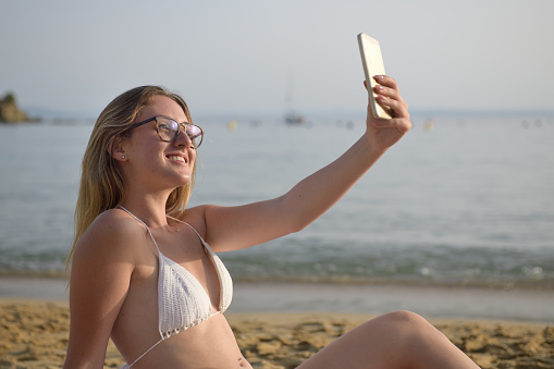 Young happy girl on the beach taking selfie with her smart phone