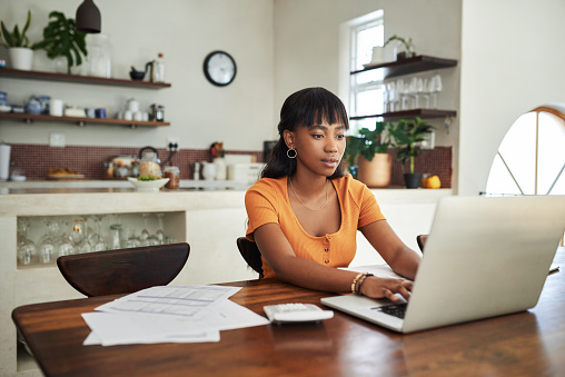 Shot of a young woman sitting with her laptop and paperwork at home