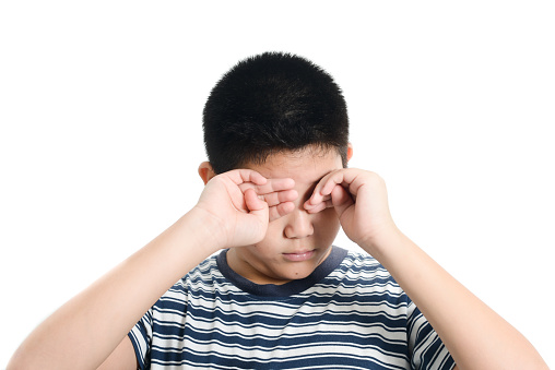 Asian preteen boy has eye pain on white background.