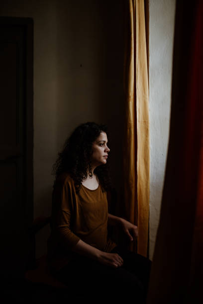 istock Thoughtful Woman Looking Through Window While Standing In Dark At Home 1159830675