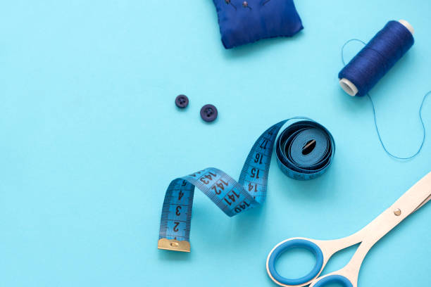 istock Sewing accessories with threads, scissors, pins, fabric, buttons and sewing tape on blue background. Top view. Flat lay. 1159833360