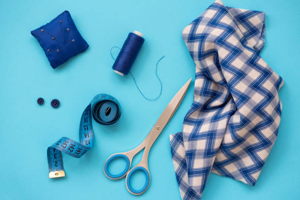istock Sewing accessories with threads, scissors, pins, fabric, buttons and sewing tape on blue background. Top view. Flat lay. 1159833584
