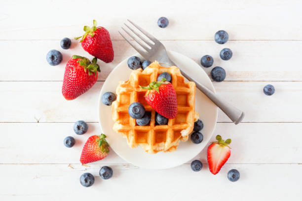 istock Breakfast waffles with strawberries and blueberries. Top view over white wood. 1159839298