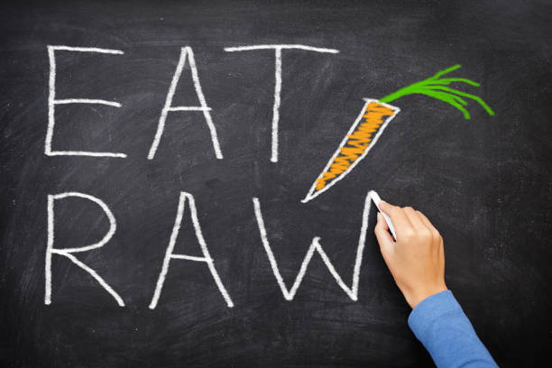 EAT RAW words written on blackboard - new trend in nutrition. The raw food diet consist of eating only uncooked, unprocessed generally vegetables and fruits, often in the form of smoothies and juices.