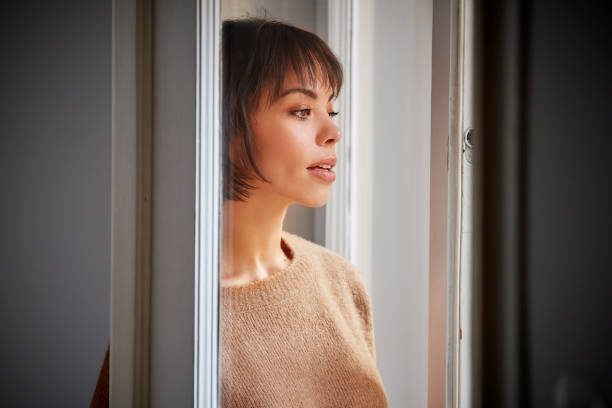 istock Beautiful woman smiling and daydreaming while standing by the window 1159843740