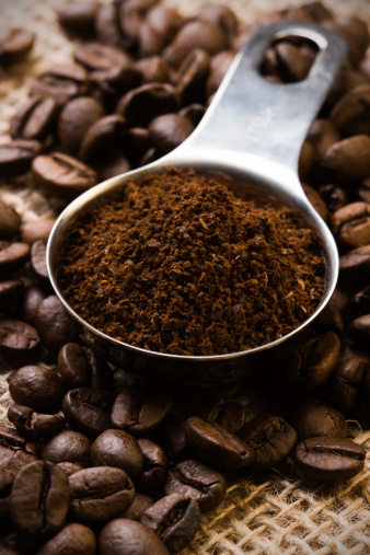 Coffee beans and ground coffee in a measuring spoon.