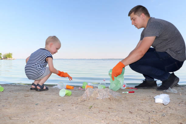A small child collects trash on the beach. His dad points his finger where to throw garbage. Parents teach children cleanliness. Clean planet concept