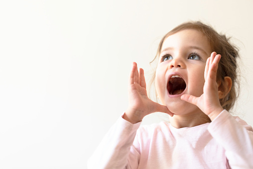 Little girl in pink clothes is shouting and is holding her hands near her mouth.