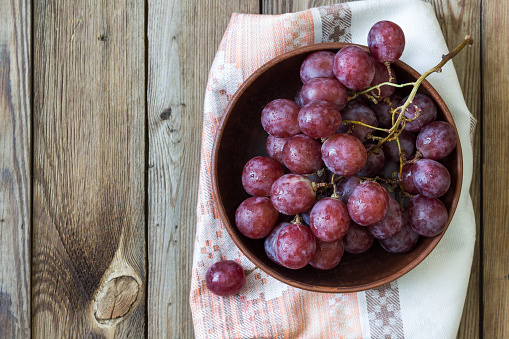 Bunch of red grapes in a bowl on a wooden table, on a light towel. Copy space