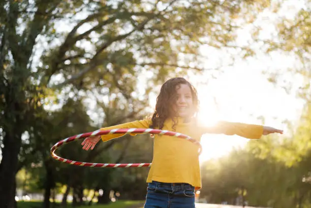 A horizontal photo of a little girl with a big smile holding her arms up beside her as she balances a stripped hula hoop.