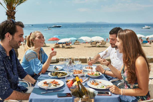 Friends Enjoying Seafood and Wine at Costa Brava Restaurant Smiling young friends enjoying seafood appetizers and wine at a sunny outdoor Costa Brava restaurant. barcelona province stock pictures, royalty-free photos & images