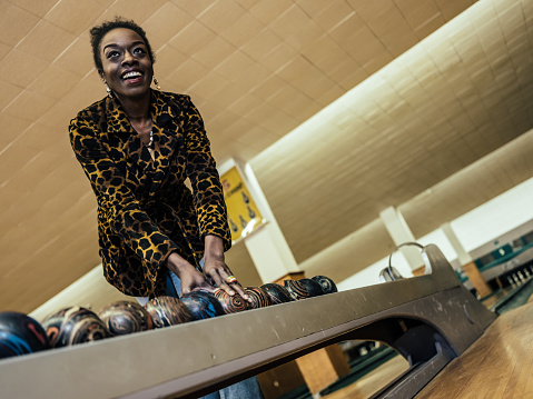 African millennial woman getting ready to roll the bowling ball, concentrating at the edge of bowling alley.