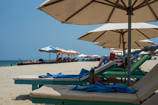 Tourists relax on long chairs under large umbrellas on a beach of Hoi An, Viet Nam.