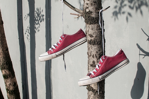 Pair of worn out vintage red old canvas sneakers hanging on their laced ties