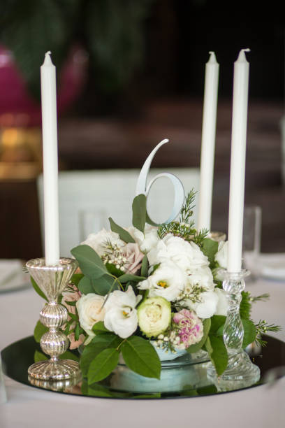 istock Wedding table setting is decorated with fresh flowers and white candles. Wedding floristry. Bouquet with roses, hydrangea and eustoma. On the background blur are burning garlands with light bulbs. 1159865040