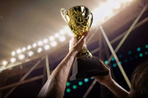 Photo of Athlete holding trophy cup above head in stadium