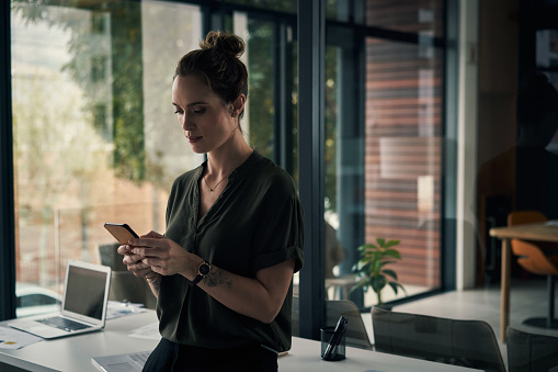 Shot of a young businesswoman using a smartphone during a late night at work