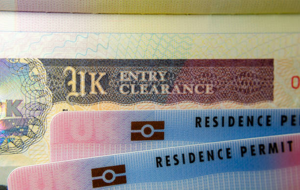 UK BRP (Biometrical Residence Permit) cards for Tier 2 work visa placed on top of UK Entry Clearance vignette sticker in the passport. stock photo