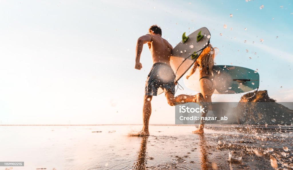 Adventures are better enjoyed together. Couple holding surfboards and running towards beach for surfing at Piha Beach, Auckland, New Zealand. Surfing Stock Photo