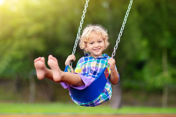 Child on playground. swing Kids play outdoor. Child playing on outdoor playground in rain. Kids play on school or kindergarten yard. Active kid on colorful swing. Healthy summer activity for children in rainy weather. Little boy swinging. swinging stock pictures, royalty-free photos & images
