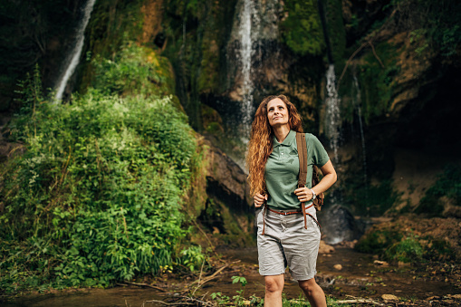 One woman, lady explorer and biologist standing in nature by waterfall alone.