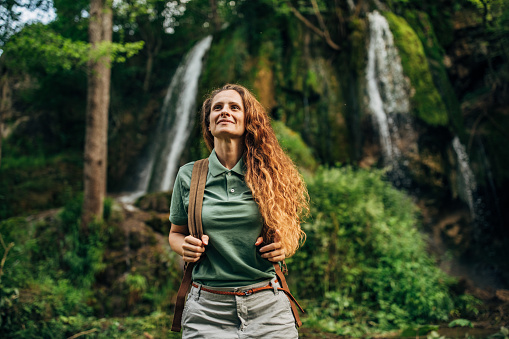 One woman, lady explorer and biologist standing in nature by waterfall alone.