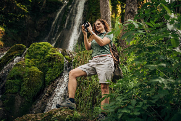 istock Lady taking pictures with camera by the waterfall 1159904185