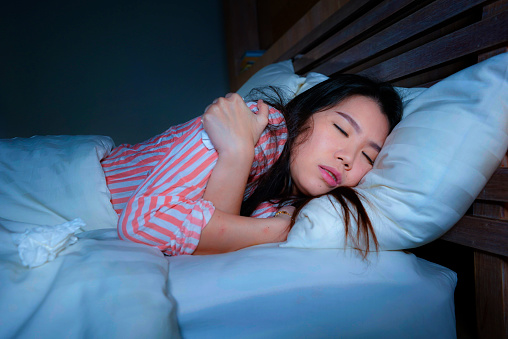 young beautiful sad and depressed Asian Chinese woman trembling in bed suffering cold and flu at night feeling unwell at night in her bedroom in health care and depression problem concept