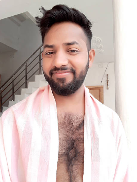 Image of young handsome Indian man with hairy chest, beard, trendy hairstyle hair quiff, naked after shower with pink towel sheet over shoulders, smiling good looking Hindi man taking selfie photo self portrait, smiling posing, looking happy carefree pose Stock photo of young handsome Indian man with hairy chest, beard, trendy hairstyle hair quiff. rockabilly hair men stock pictures, royalty-free photos & images