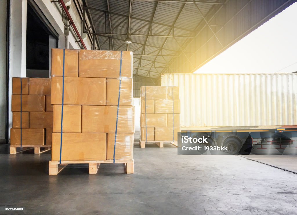 Warehouse cargo courier shipment. Stack of cardboard boxes on wooden pallet and truck docking at warehouse Warehouse cargo courier transportation Freight Transportation Stock Photo