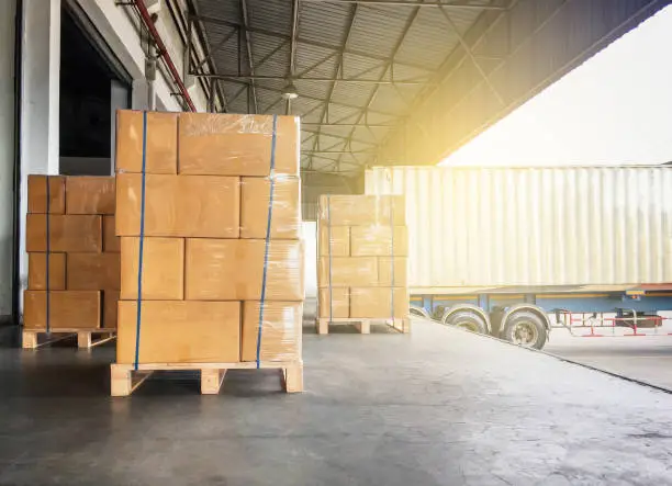 Photo of Warehouse cargo courier shipment. Stack of cardboard boxes on wooden pallet and truck docking at warehouse