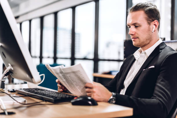 istock Confident young handsome businessman reading newspaper and working with computer in modern office 1159939201