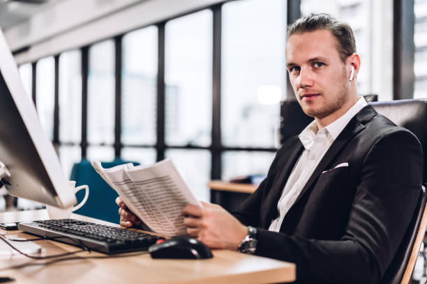 istock Confident young handsome businessman reading newspaper and working with computer in modern office 1159939204