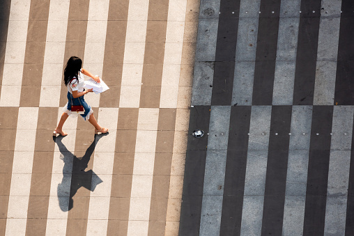 Chengdu, Sichuan province, China - June 12, 2019 : Young chinese woman walking on a zebra crossing aerial top view on a sunny day