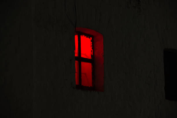 istock Window with burning red light in the night dark 1159946282