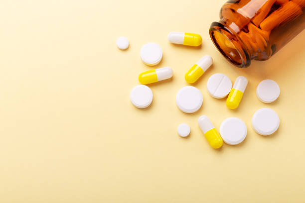 istock Multicolor tablets and pills capsules from glass bottle on yellow background Close-up 1159946344
