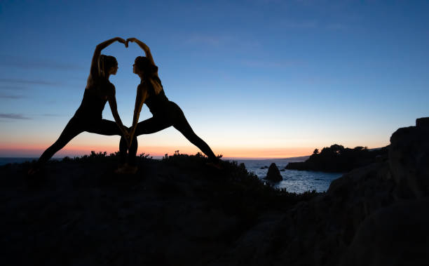 Mother and daughter creating heart doing yoga by ocean at sunset Woman doing yoga by ocean at sunset in California i love you photos stock pictures, royalty-free photos & images
