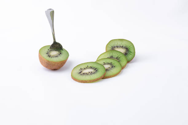 Four green slices with seeds, accompanied by a kiwi cut in half with a spoon on a white background - Fresh kiwi - Top view