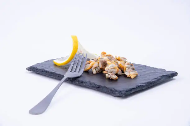Photo of Close-up of marine appetizers - Tasty cockles and lemon served on a black rustic stone board