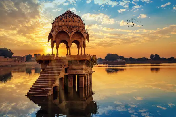 Ancient architecture ruins at Gadi Sagar (Gadisar) lake Jaipur Rajasthan at sunrise with vibrant moody sky.