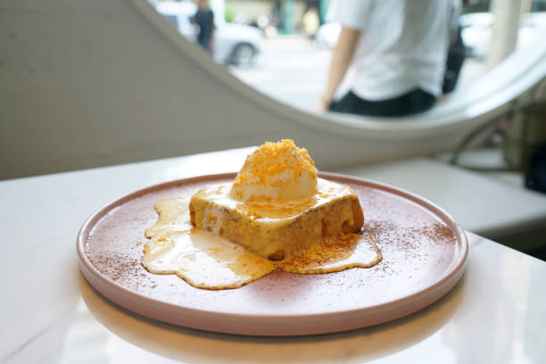 un plato de tostadas francesas (perdu de dolor) con salsa de huevo de yema salada, cubierto con helado de vainilla y copos de yema de huevo sobre mesa de mármol y fondo borroso. - pan perdu fotografías e imágenes de stock