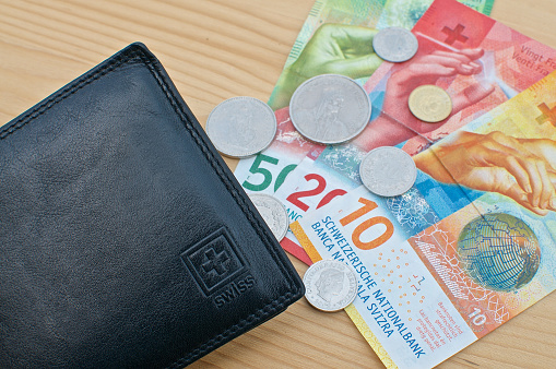 Top view of a black wallet and Swiss currency on a wooden table