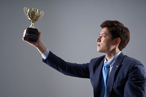 korean ethnicity businessman sitting holding a golden trophy