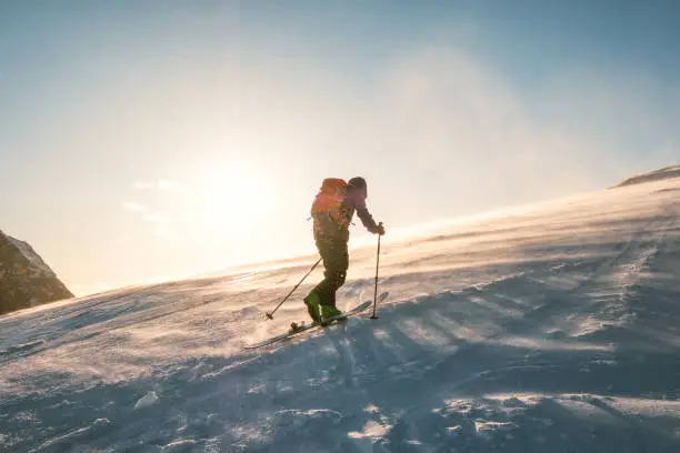 Man skier with backpack trekking on snow mountain with sunlight and storm