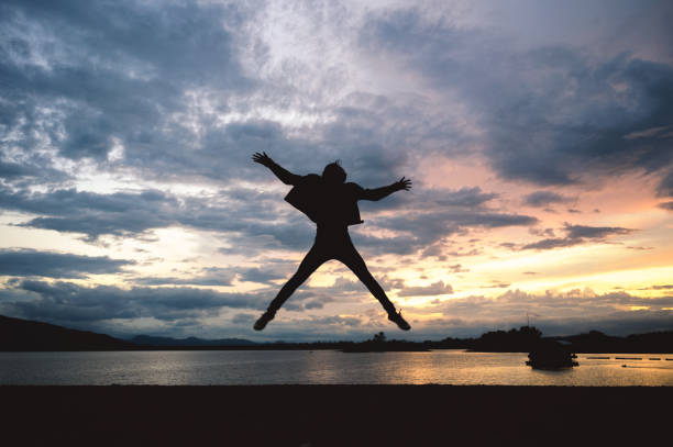 istock Silhouette happiness man jumping on lake at sunset 1159960121