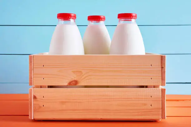 Photo of Traditional milk bottles in a wooden crate on wooden kitchen table with blue wooden background.