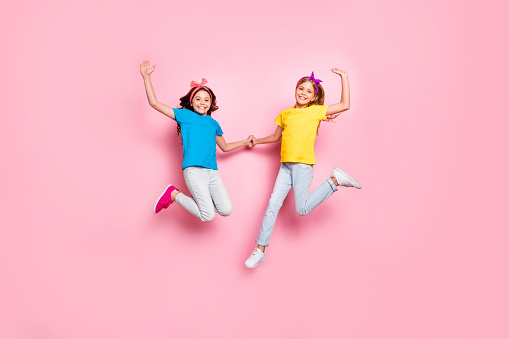 Full size photo of lovely kids raise hands have free time wear t-shirt pants, trousers isolated over pink background