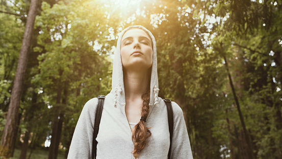 Relaxed young woman walking in nature and feeling relaxed, sunlight shining through trees, relax and mindfulness concept
