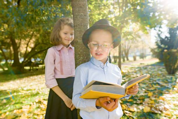 niño de 6,7 años con sombrero, gafas, libro de lectura y niña de 7,8 años - eyewear child glasses 6 7 years fotografías e imágenes de stock