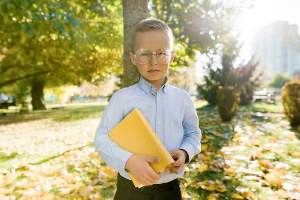 niño de 6, 7 años en gafas con libro en otoño parque soleado, hora dorada - eyewear child glasses 6 7 years fotografías e imágenes de stock